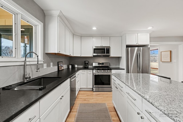 kitchen featuring sink, light hardwood / wood-style flooring, light stone countertops, appliances with stainless steel finishes, and white cabinetry