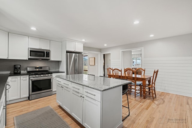 kitchen featuring a center island, white cabinets, light wood-type flooring, light stone countertops, and stainless steel appliances