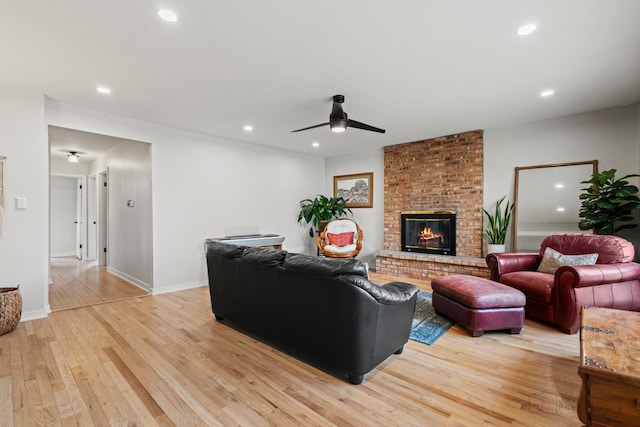 living room featuring ceiling fan, light wood-type flooring, and a fireplace