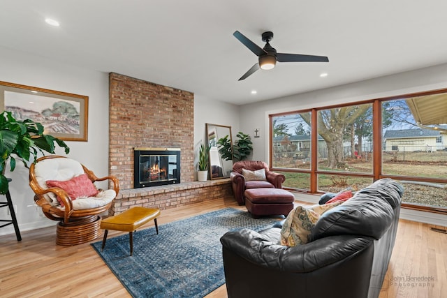 living room featuring hardwood / wood-style flooring, ceiling fan, and a fireplace