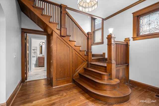 stairway featuring wood-type flooring, a healthy amount of sunlight, and ornamental molding