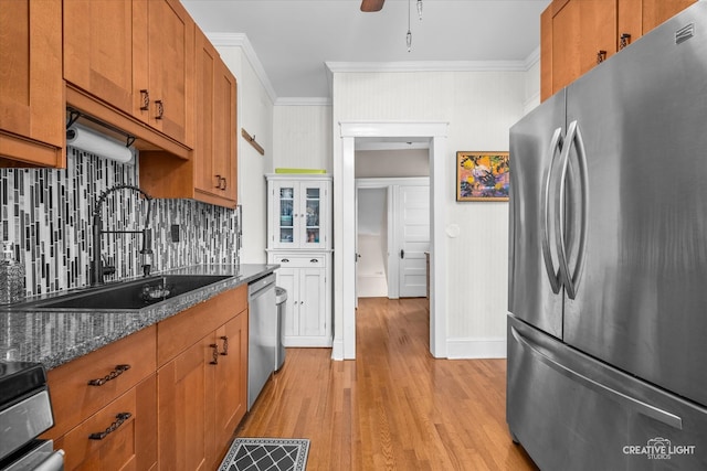 kitchen with stainless steel appliances, sink, crown molding, light hardwood / wood-style flooring, and dark stone countertops