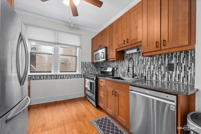 kitchen featuring stainless steel appliances, sink, dark stone counters, light hardwood / wood-style flooring, and crown molding