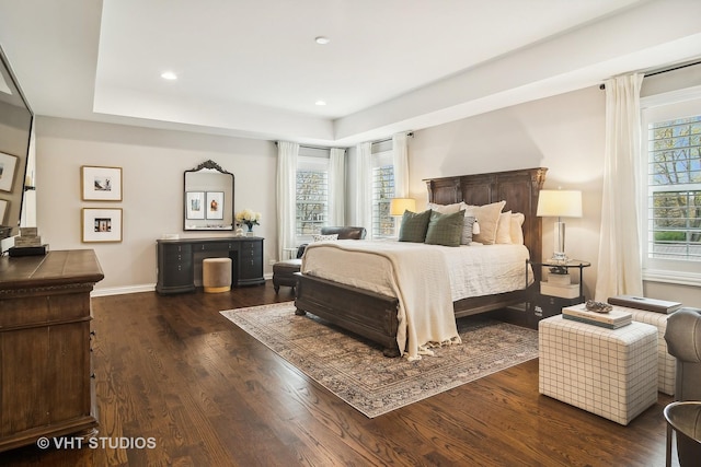 bedroom with dark wood-type flooring, a tray ceiling, and multiple windows