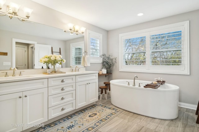 bathroom with vanity, a notable chandelier, and a tub to relax in