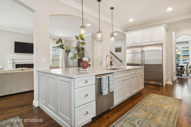 kitchen featuring decorative light fixtures, white cabinetry, sink, stainless steel appliances, and a center island with sink