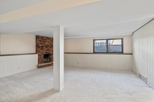 basement featuring light colored carpet, a brick fireplace, and wood walls