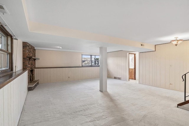 basement with light colored carpet, a brick fireplace, and wood walls