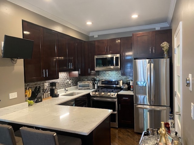 kitchen with kitchen peninsula, a kitchen bar, dark wood-type flooring, crown molding, and stainless steel appliances