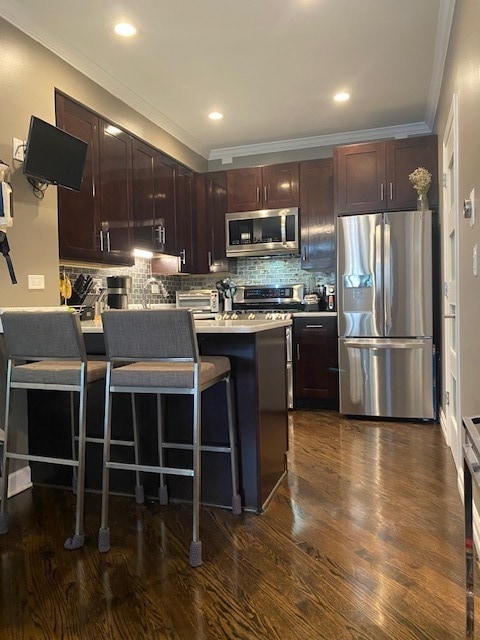 kitchen featuring backsplash, stainless steel appliances, ornamental molding, a breakfast bar area, and dark hardwood / wood-style floors