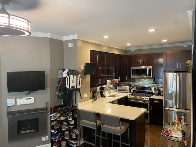 kitchen featuring appliances with stainless steel finishes, a kitchen bar, kitchen peninsula, ornamental molding, and dark hardwood / wood-style floors