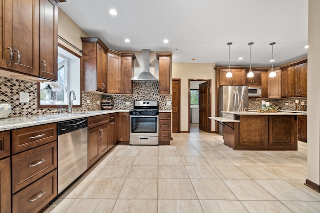 kitchen featuring light stone countertops, stainless steel appliances, wall chimney range hood, pendant lighting, and light tile patterned floors