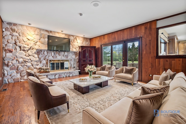 living room with french doors, light wood-type flooring, a stone fireplace, and wood walls