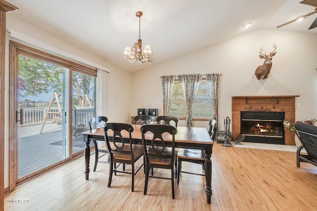 dining space with a fireplace, ceiling fan with notable chandelier, light hardwood / wood-style floors, and lofted ceiling