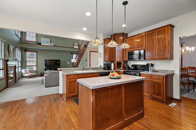 kitchen with sink, black appliances, light wood-type flooring, a center island, and pendant lighting