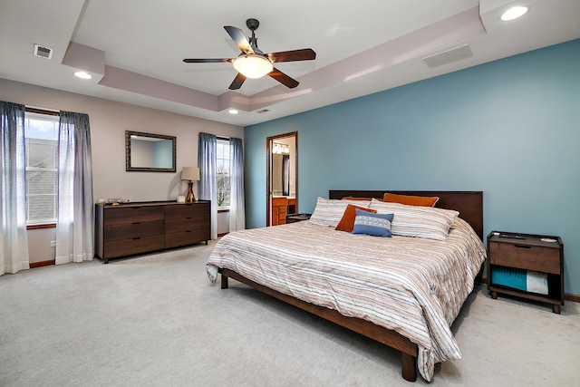 bedroom with multiple windows, light carpet, ceiling fan, and a raised ceiling