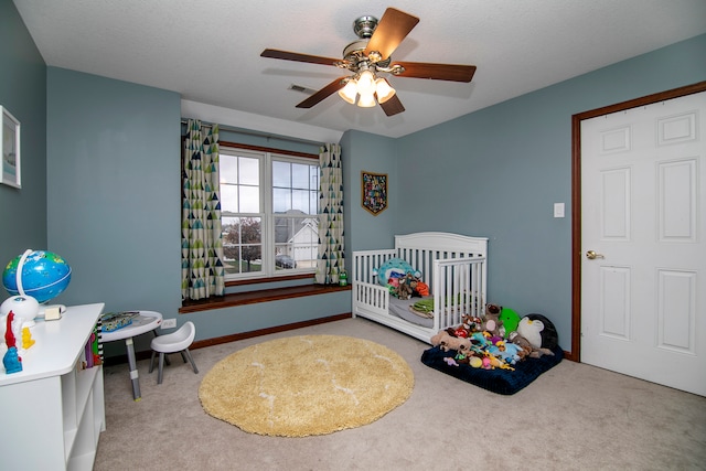 bedroom featuring a nursery area, a textured ceiling, carpet, and ceiling fan