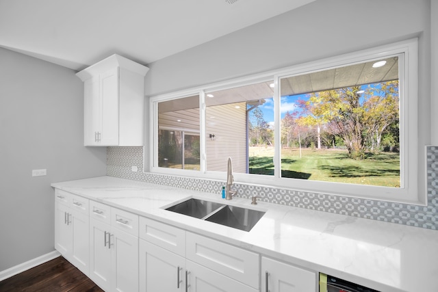 kitchen with tasteful backsplash, light stone counters, white cabinetry, dark wood-type flooring, and sink