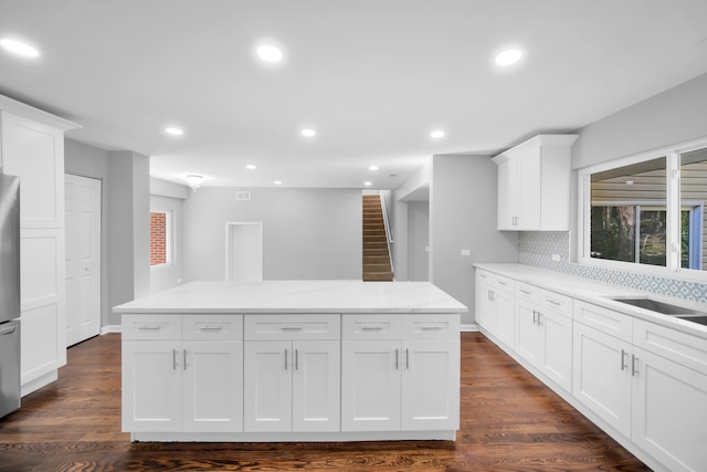 kitchen with decorative backsplash, white cabinets, light stone counters, dark hardwood / wood-style floors, and a center island