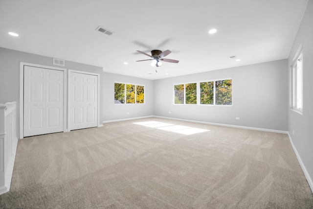 unfurnished bedroom featuring light carpet, multiple closets, and ceiling fan