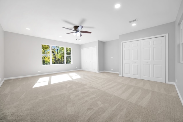 unfurnished bedroom with multiple closets, light colored carpet, and ceiling fan