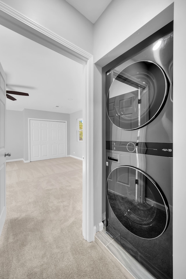 laundry room featuring stacked washer / drying machine, light colored carpet, and ceiling fan