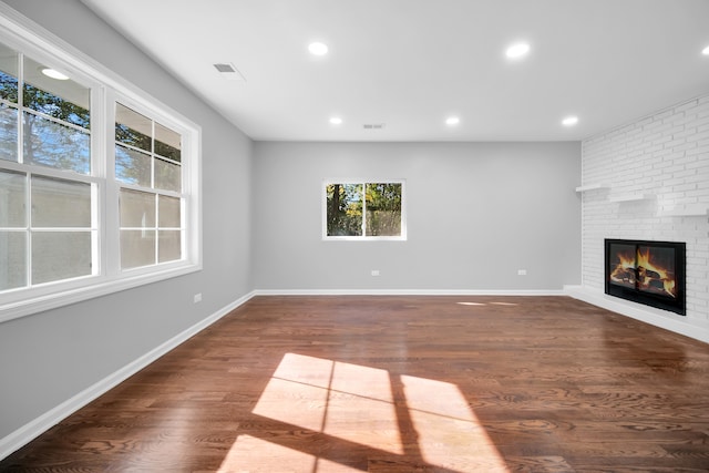 unfurnished living room featuring dark wood-type flooring and a brick fireplace