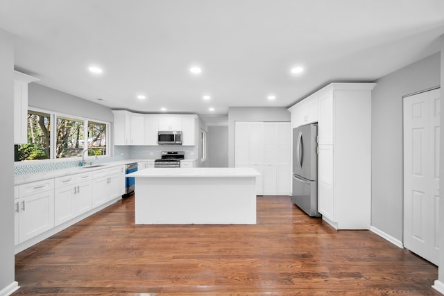 kitchen with appliances with stainless steel finishes, white cabinetry, dark wood-type flooring, and a kitchen island