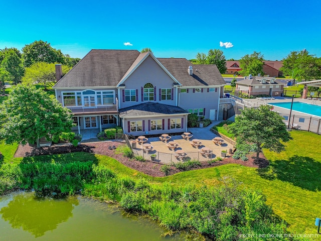 rear view of house with a patio, a fenced in pool, a lawn, and a water view