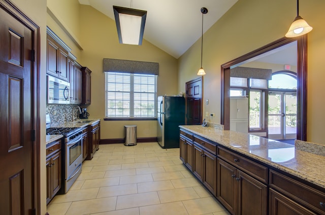 kitchen with a wealth of natural light, appliances with stainless steel finishes, pendant lighting, and light stone countertops