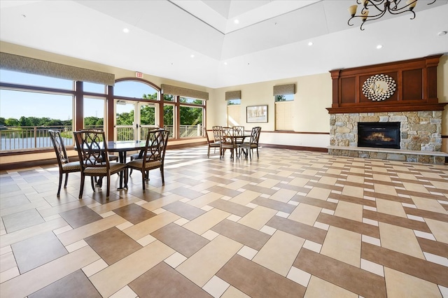 dining area with a stone fireplace, an inviting chandelier, and a high ceiling