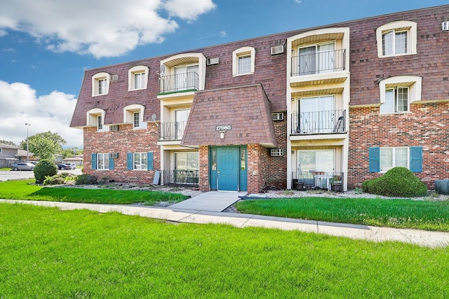 view of front of house featuring a front yard, a balcony, and a wall mounted air conditioner