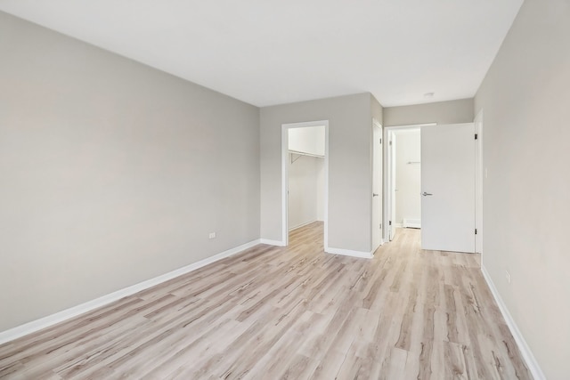 unfurnished bedroom featuring a closet, a baseboard radiator, light wood-type flooring, and a walk in closet