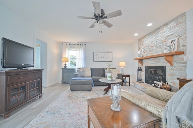 living room featuring light hardwood / wood-style floors, a stone fireplace, and ceiling fan