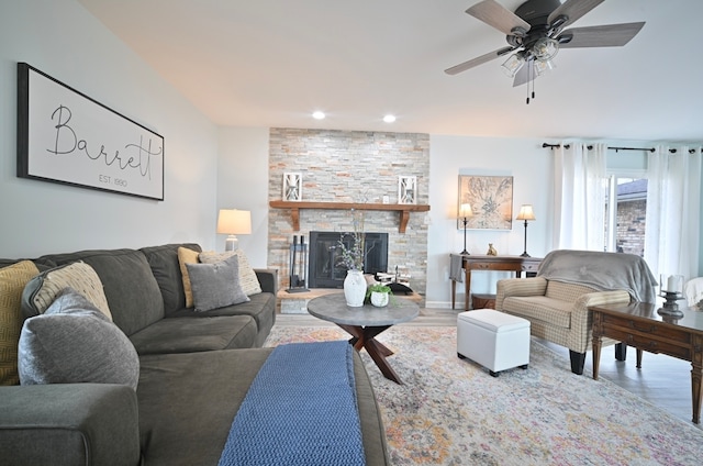 living room featuring a stone fireplace, wood-type flooring, and ceiling fan