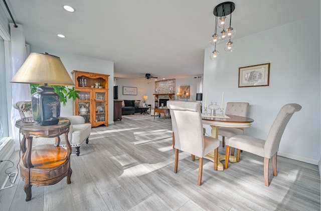 dining area with a fireplace, light wood-type flooring, and ceiling fan