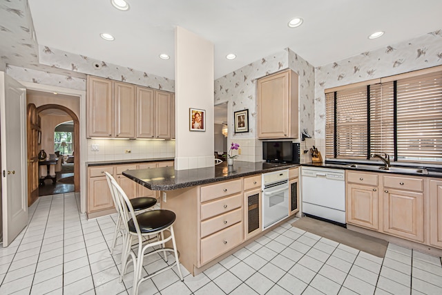 kitchen featuring kitchen peninsula, a breakfast bar area, dark stone counters, sink, and white appliances