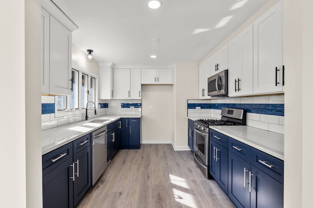 kitchen with sink, blue cabinets, white cabinetry, light hardwood / wood-style floors, and stainless steel appliances