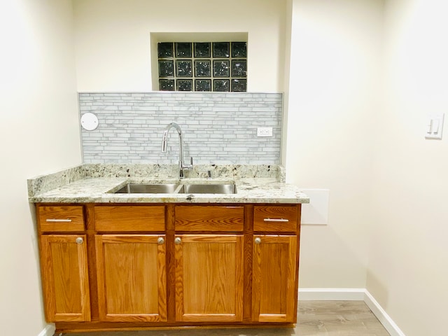 kitchen with light hardwood / wood-style flooring, tasteful backsplash, sink, and light stone counters