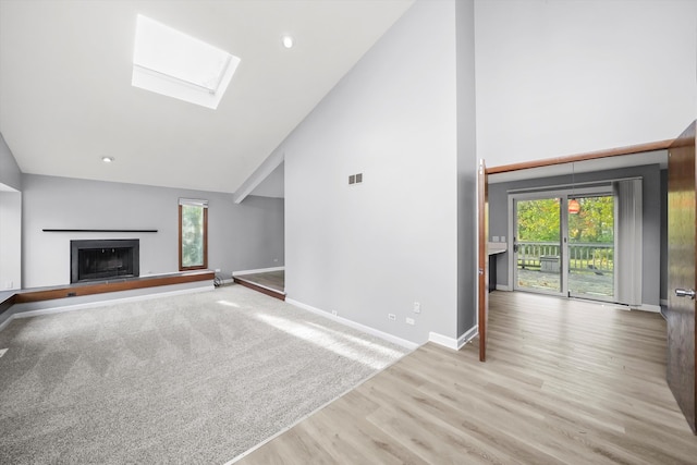 unfurnished living room with light hardwood / wood-style flooring, high vaulted ceiling, and a skylight