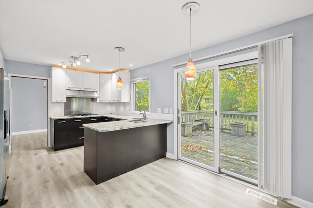 kitchen with kitchen peninsula, light hardwood / wood-style floors, decorative light fixtures, white cabinets, and light stone counters