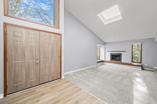 unfurnished living room featuring light hardwood / wood-style floors, high vaulted ceiling, and a skylight