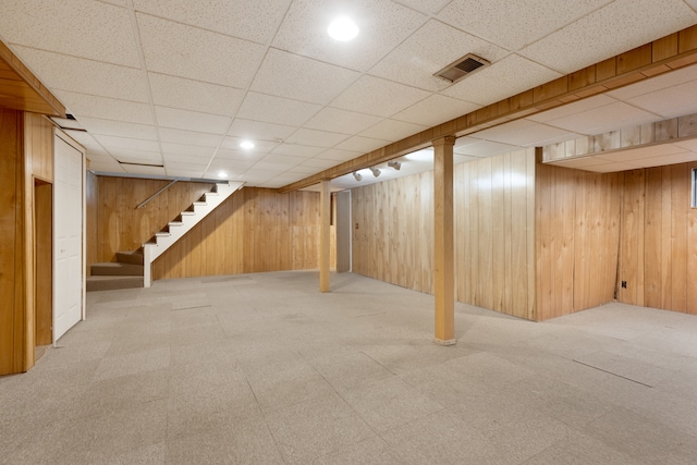 basement featuring a drop ceiling and wood walls