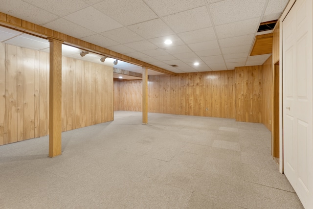 basement featuring a drop ceiling, wooden walls, and light colored carpet