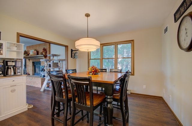 dining area with dark wood-type flooring and a brick fireplace