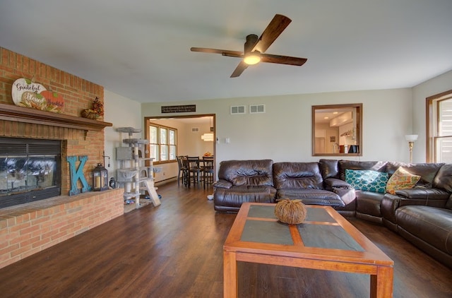 living room featuring a brick fireplace, dark hardwood / wood-style floors, a healthy amount of sunlight, and ceiling fan