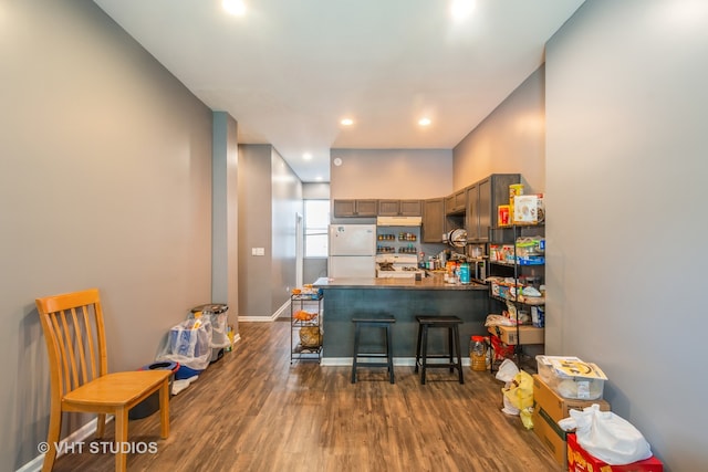 kitchen featuring a breakfast bar area, kitchen peninsula, dark hardwood / wood-style floors, and white refrigerator