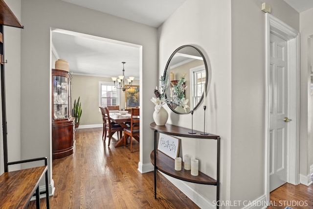 corridor featuring ornamental molding, an inviting chandelier, wood finished floors, and baseboards