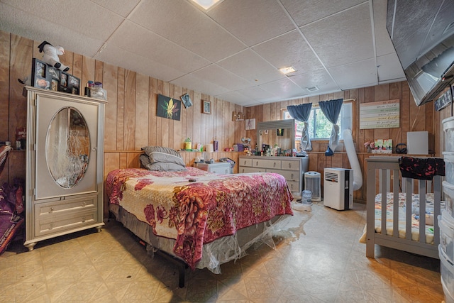 bedroom featuring a drop ceiling and wood walls