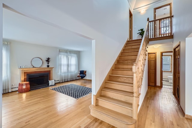 stairway with wood-type flooring, a fireplace, and a baseboard heating unit